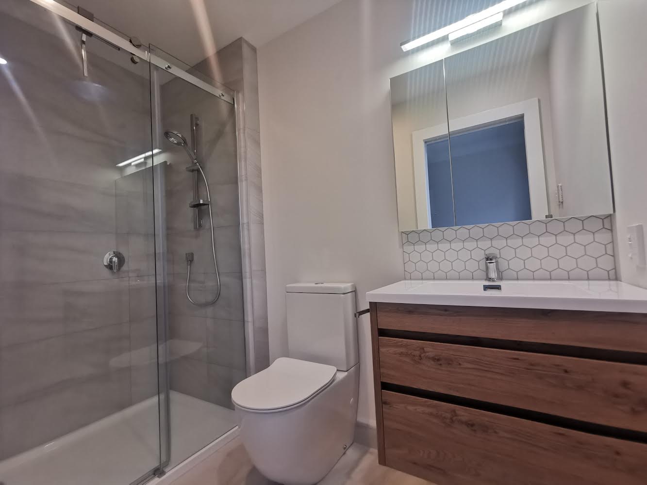 Bathroom addition Auckland — wardrobe converted to ensuite with sliding glass shower, hexagonal mosaic and timber vanity