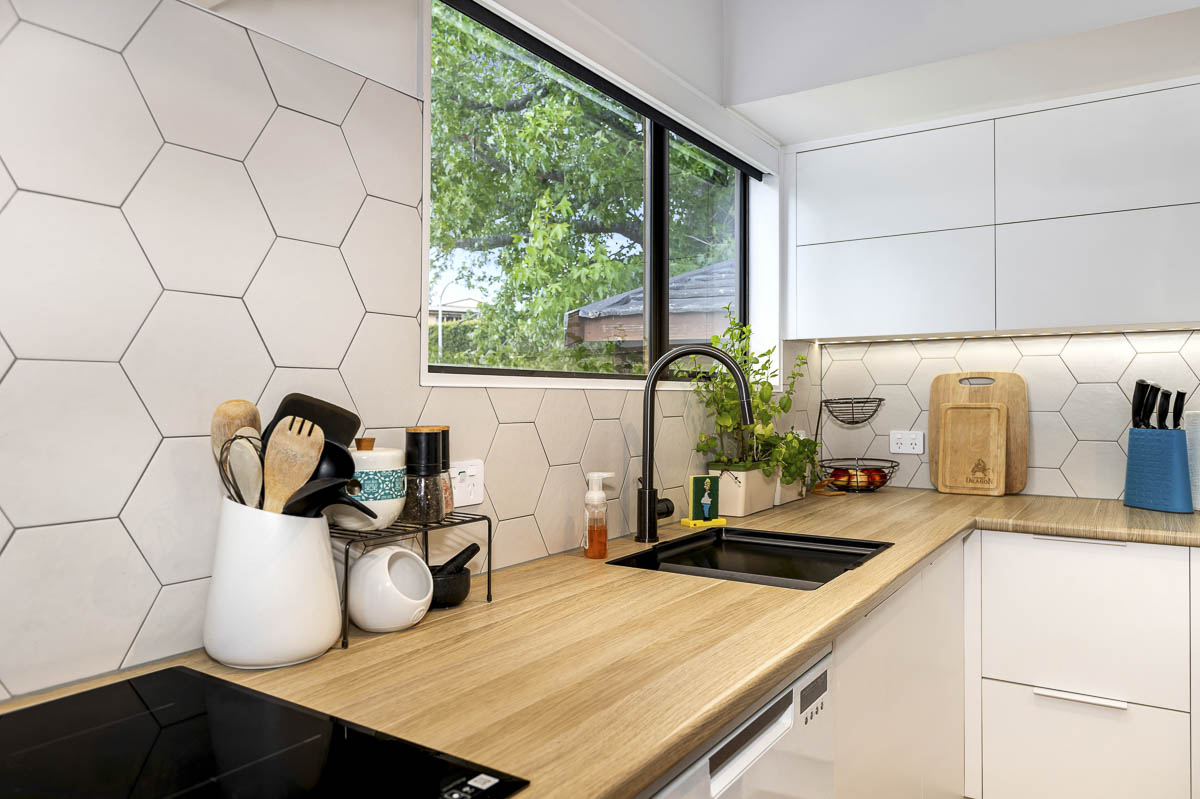 Galley compact kitchen renovation Auckland with white hexagonal feature tile, timber benchtop and handle-less white cabinetry