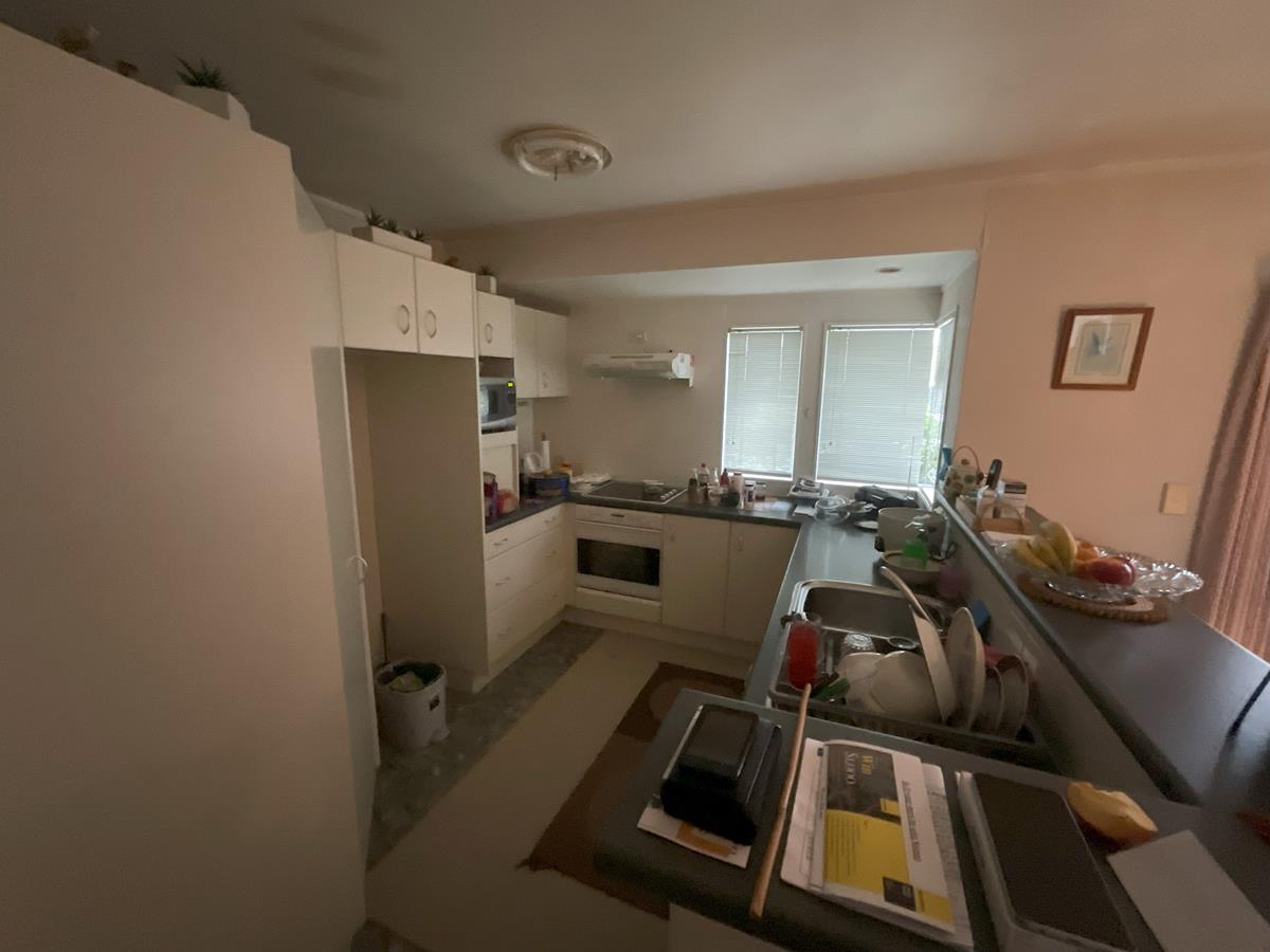 Before — old U-shaped kitchen with outdated white cabinetry awaiting renovation — Mt Roskill home before AVR renovation